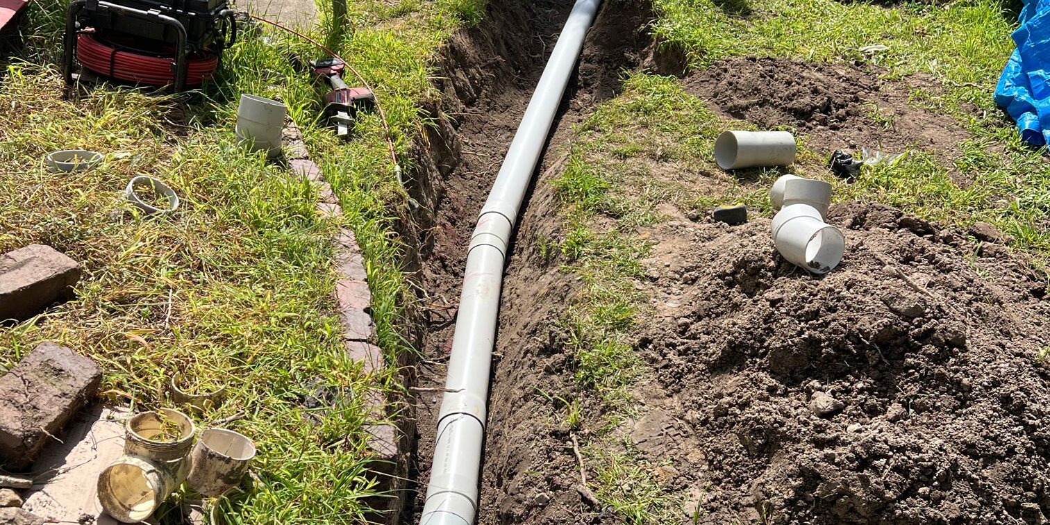 4a34692b-938a-4e2d-84e0-249f7b184f7a_0 New 100 mm PVC stormwater pipe laid in an open trench across a back lawn in Eden NSW