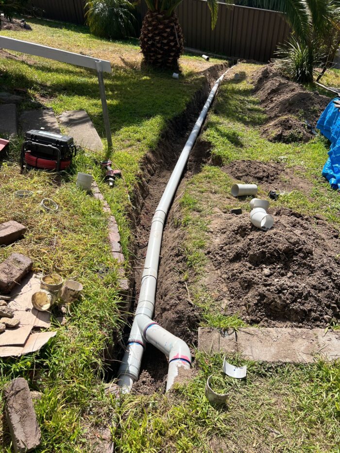New 100 mm PVC stormwater pipe laid in an open trench across a back lawn in Eden NSW