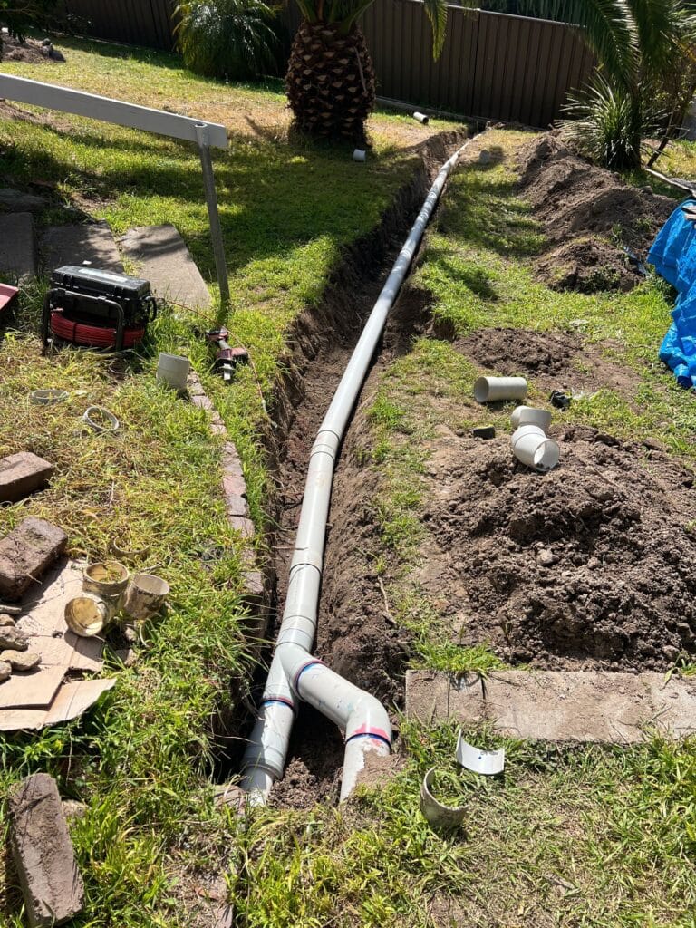 4a34692b-938a-4e2d-84e0-249f7b184f7a_0 New 100 mm PVC stormwater pipe laid in an open trench across a back lawn in Eden NSW