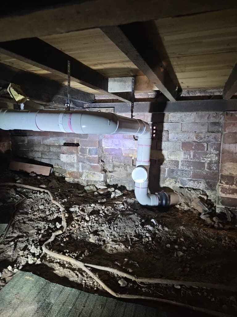 Photo (1) New PVC stormwater pipe suspended from floor joists on galvanised strap hangers under a house