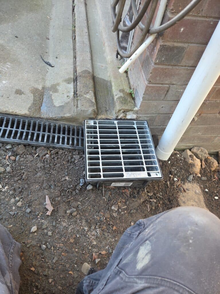Photo (2) New 300 x 300 mm stormwater sump pit with a galvanised steel grate installed beside a channel drain