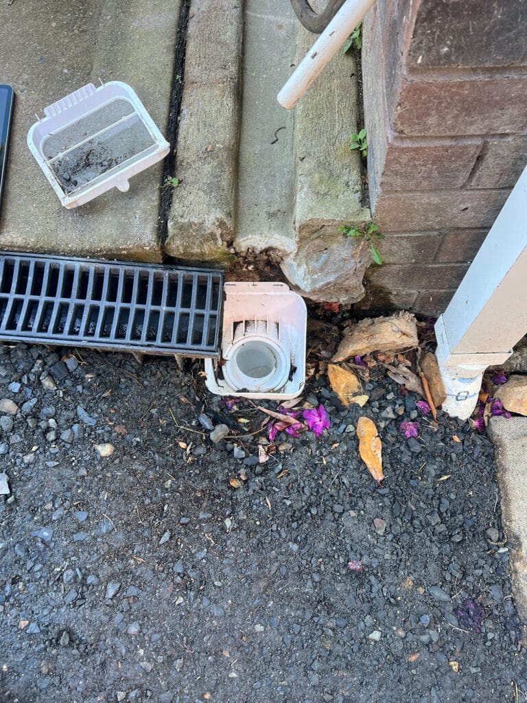 e91d9cf2-4278-415a-8c69-249d2c33d7fa_0 Silted leaf basket and a loose stormwater outlet beside a channel drain before the new sump went in